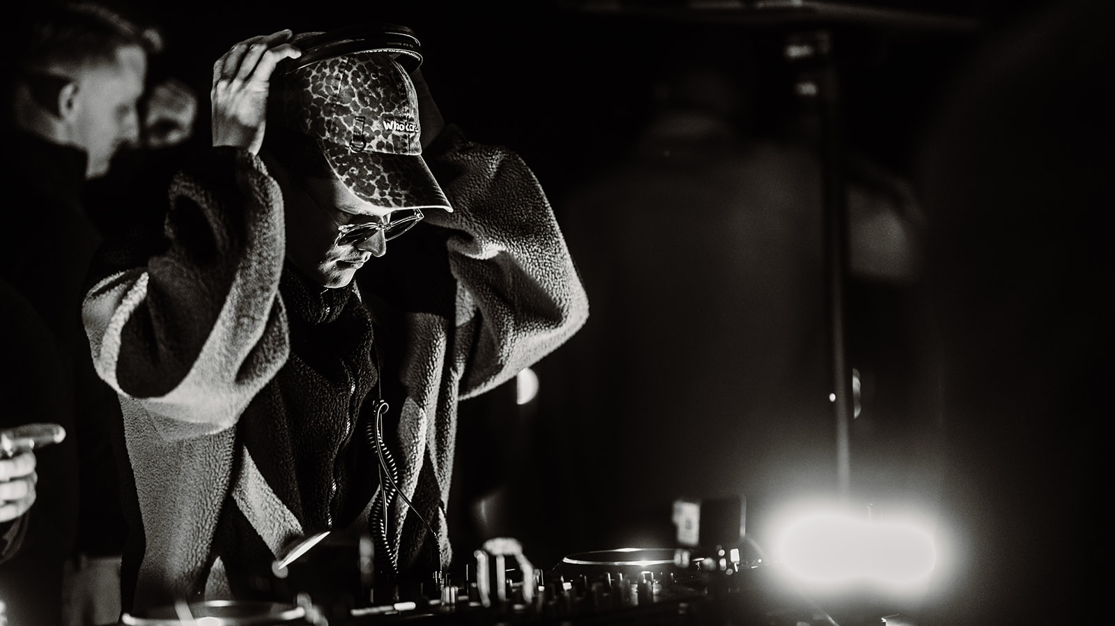 DJ adjusting the cap behind the decks in low light — Bisou.at, photographed by Paul Rumplmaier