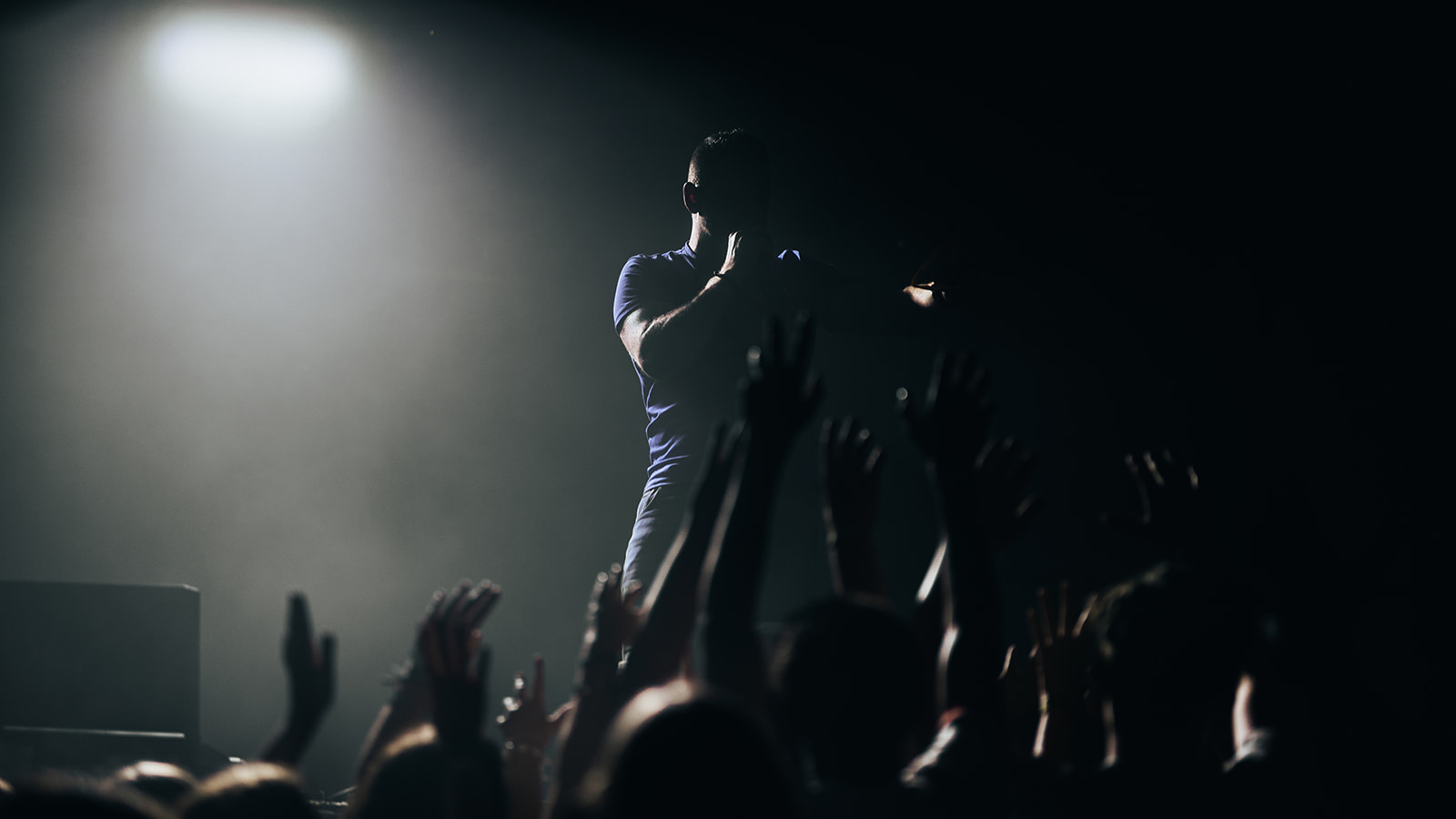 Artist above a sea of raised hands in a single spotlight — Best of, photographed by Paul Rumplmaier