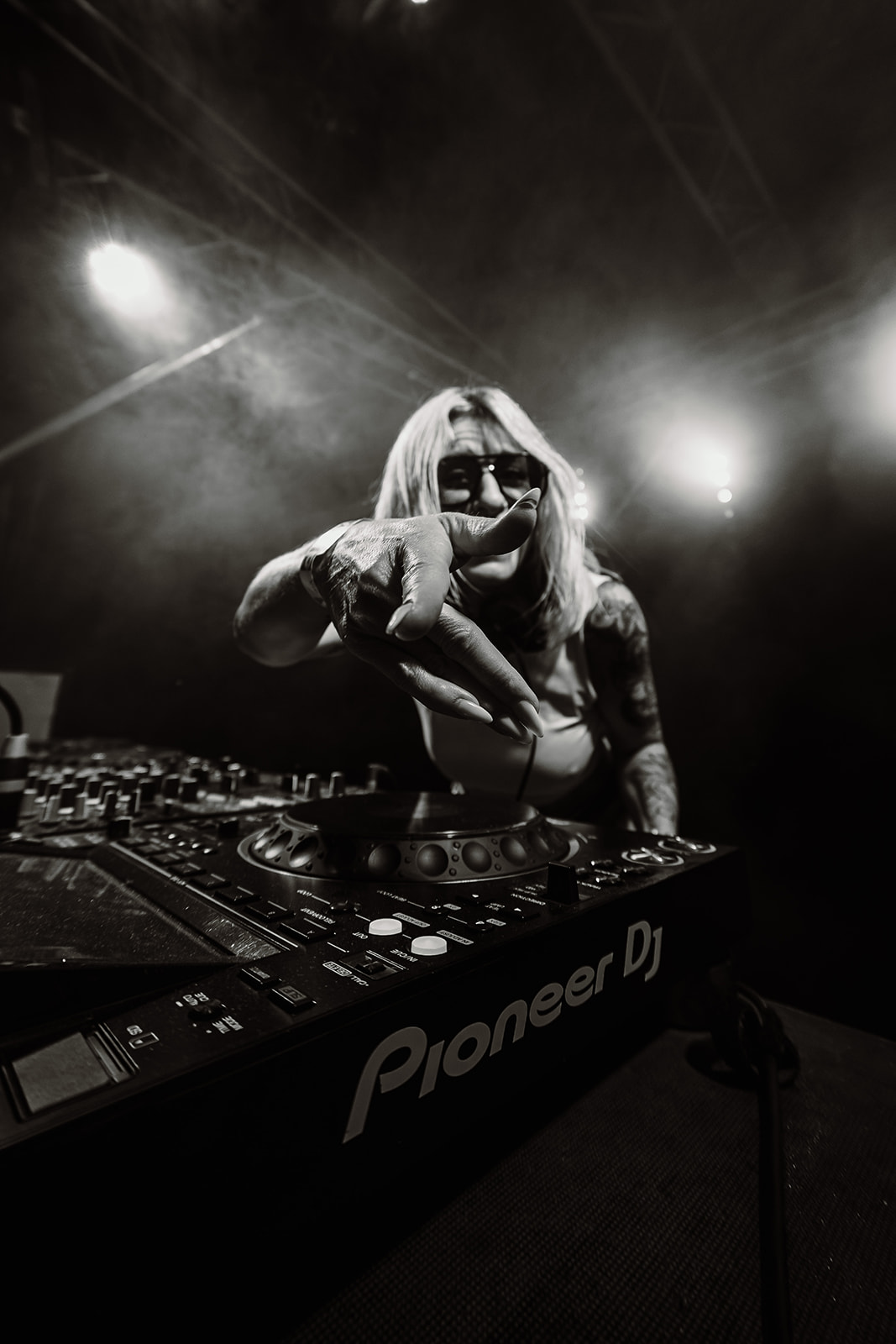 Black and white portrait of a DJ reaching towards the camera over the mixer — Best of, photographed by Paul Rumplmaier