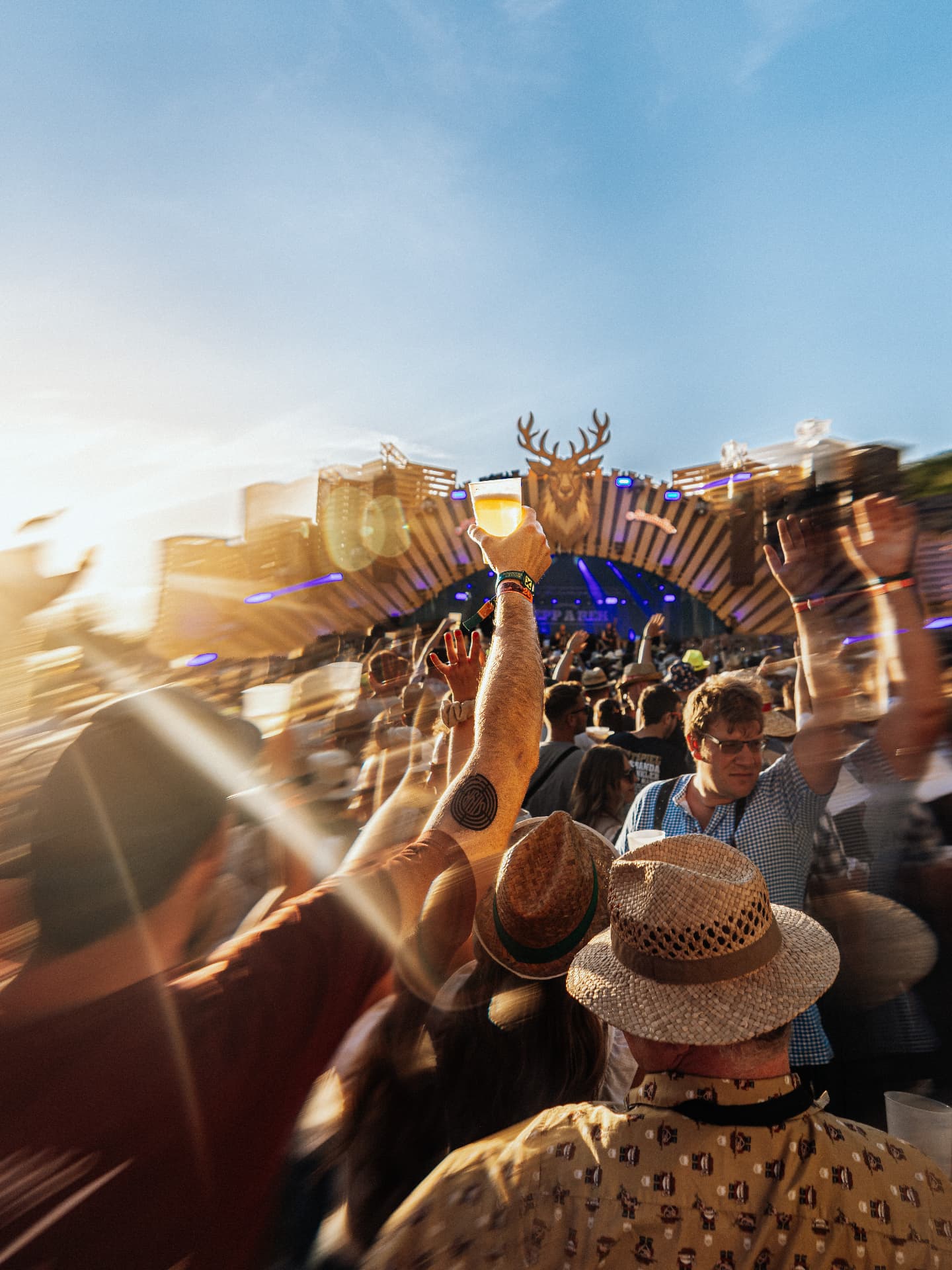 Festival visitor raising a beer towards the stage in the evening sun — Woodstock der Blasmusik, photographed by Paul Rumplmaier