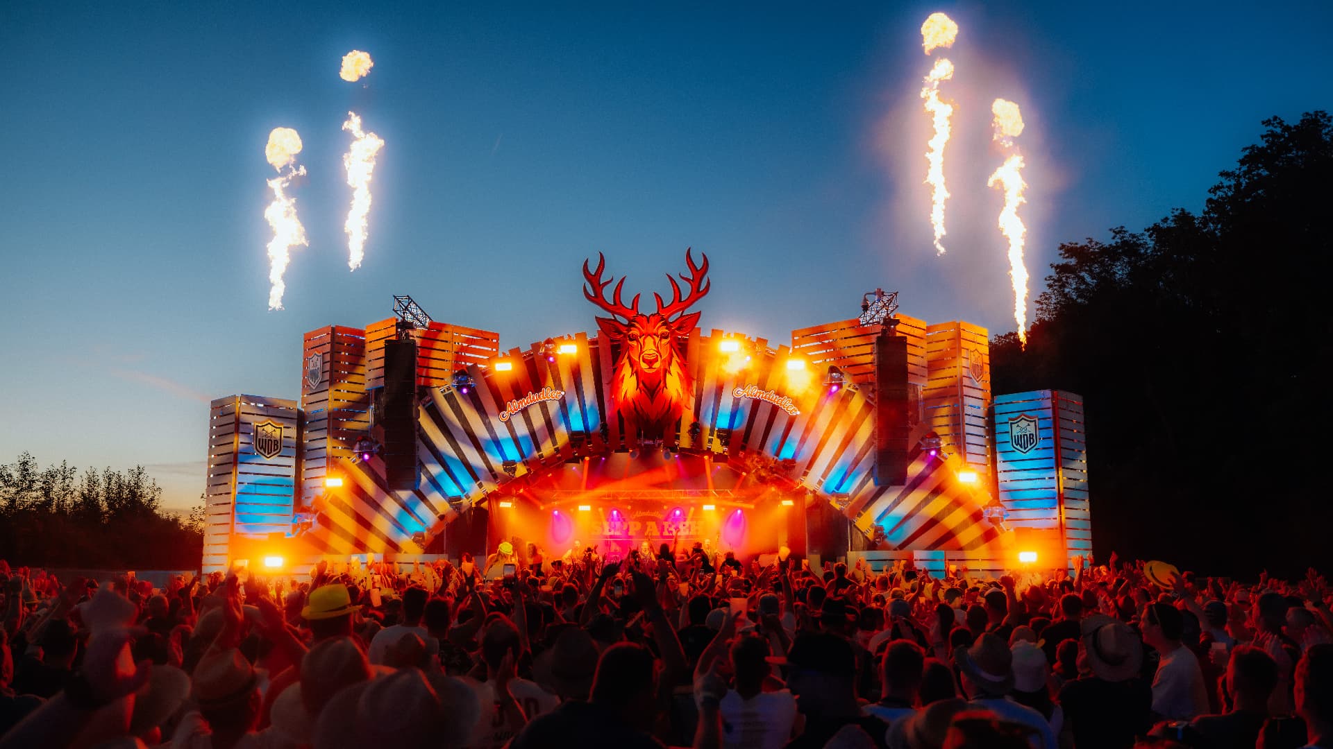 Main stage at dusk with flame jets above a packed crowd — Woodstock der Blasmusik, photographed by Paul Rumplmaier